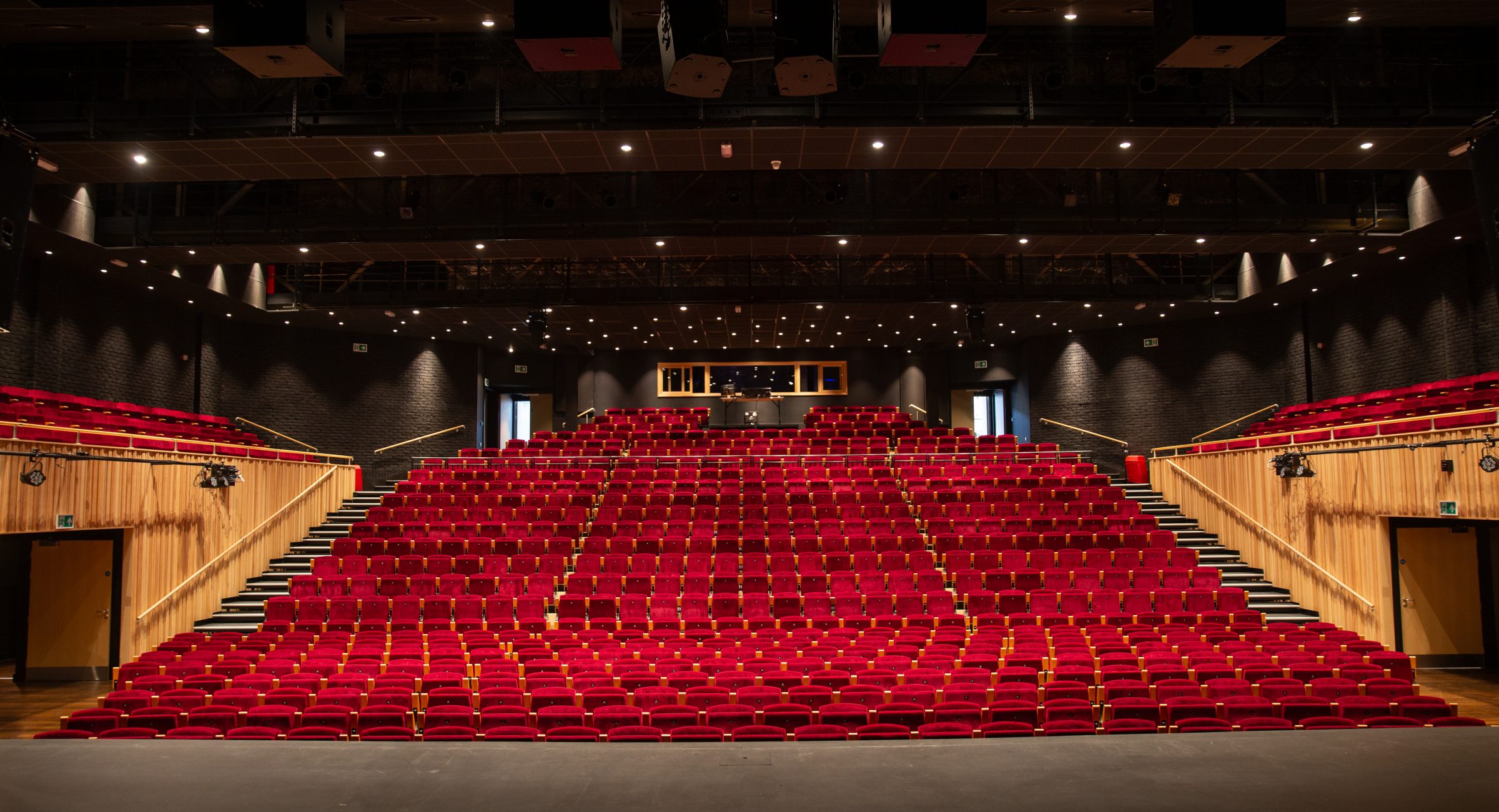 The auditorium featuring dark grey stage and red tiered seating and the lighting rig visible.