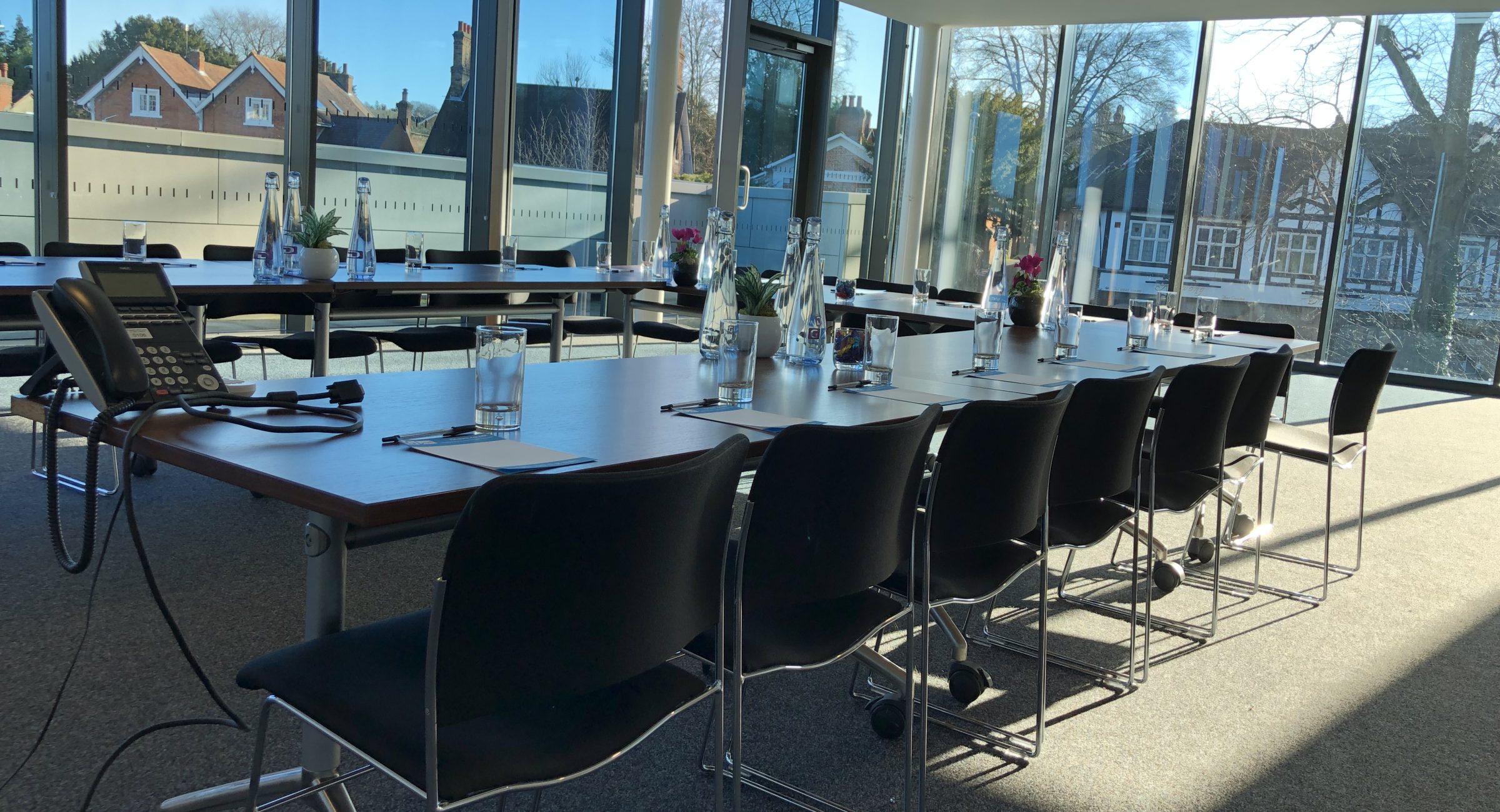 A boardroom layout of a long table in a U shape, with a phone and water glasses and glass bottles on.
