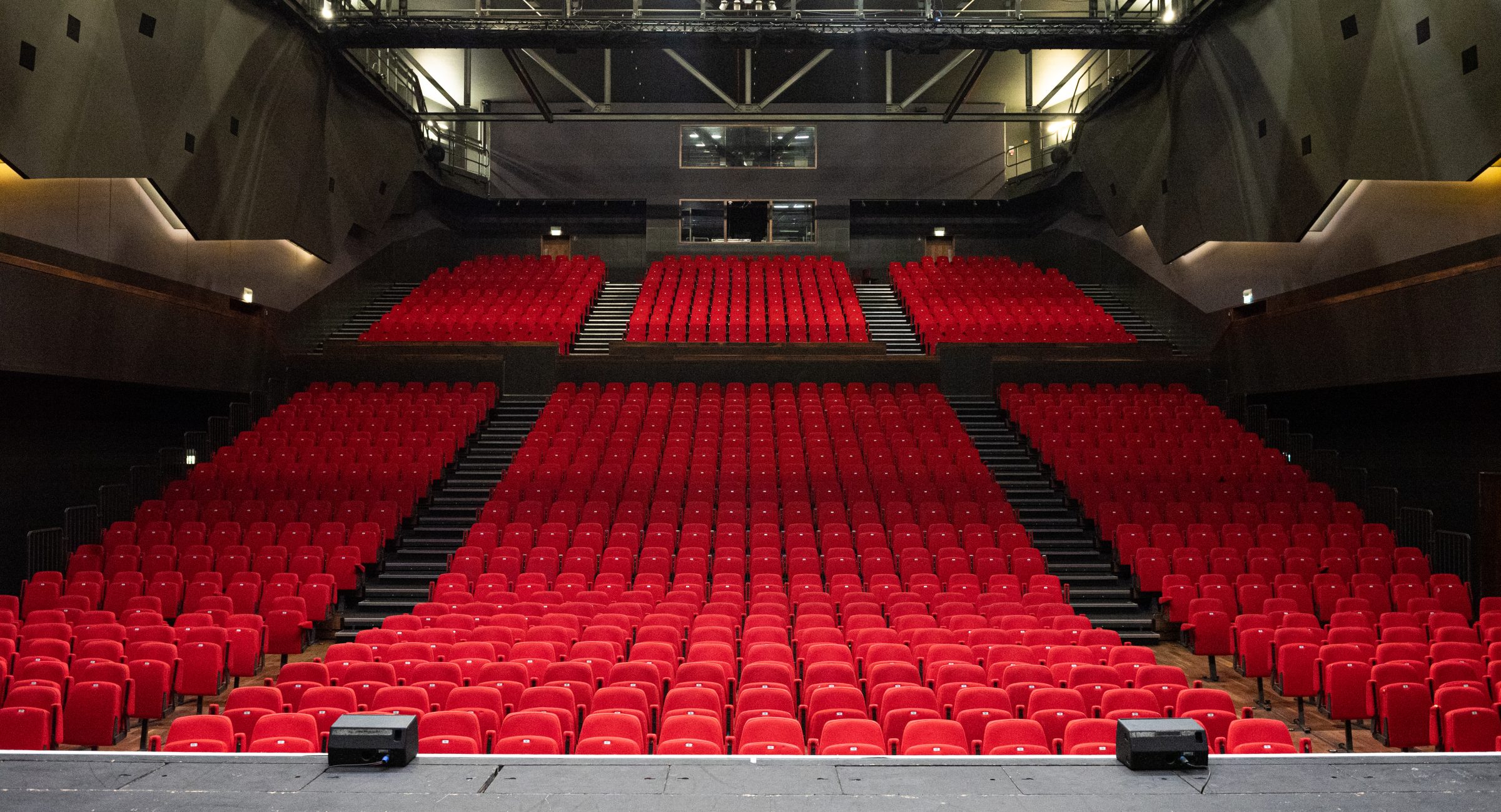 A shot from centre stage of the auditorium with tiered red seats and the lighting rig at the top.