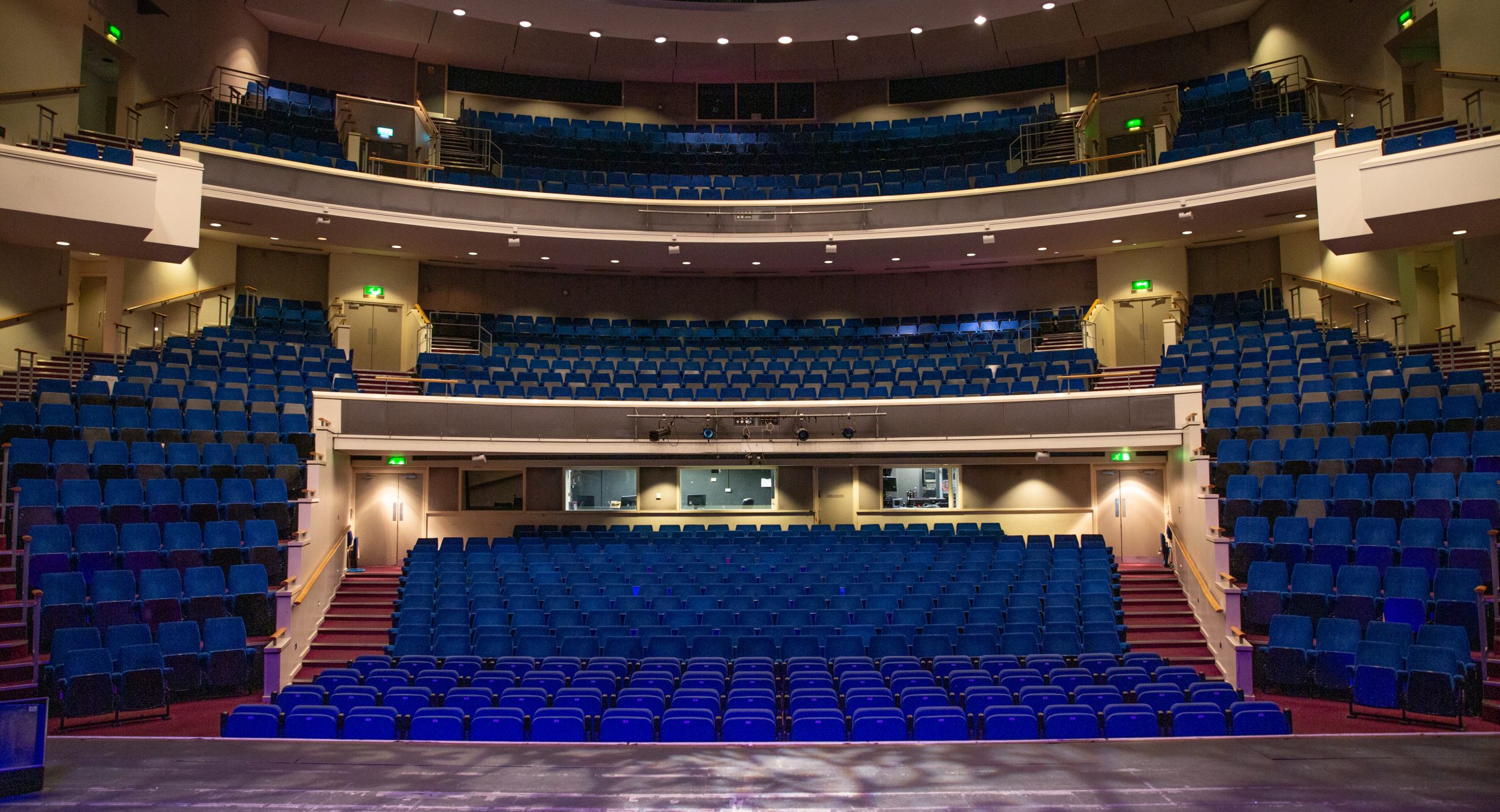 Stage centre shot out onto a brighltly lit auditorium with tiered leveled blue seats.