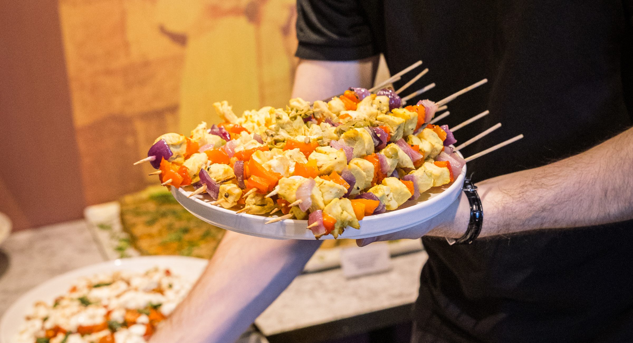 A staff member placing serving plates of skewers on a marble table.