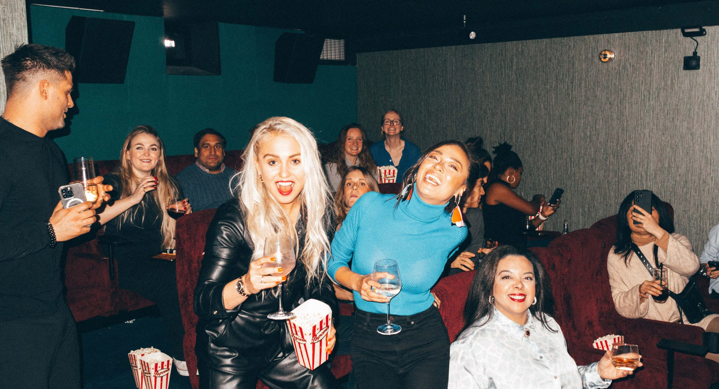 A laughing picture of guests with drinks in the smallest screen in the cinema with dark red seats.